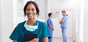 Portrait Of Smiling Female Doctor Wearing Scrubs In Hospital Corridor Holding Digital Tablet